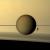 I globi di Titano e Dione si stagliano sul profilo degli anelli di Saturno; sotto, l’ombra striata degli anelli sull’atmosfera del pianeta. 